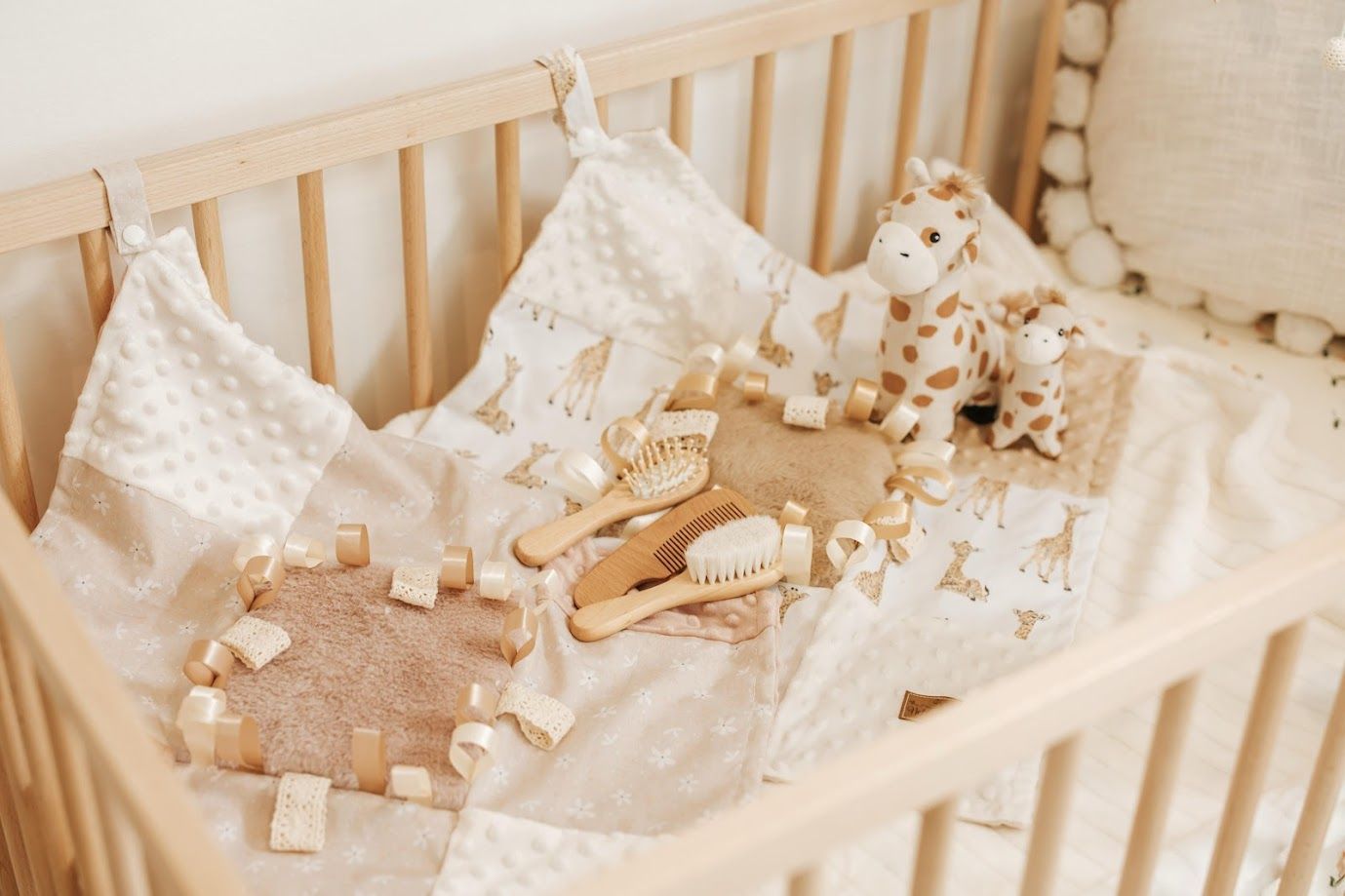 Wooden baby crib with soft white blankets, a giraffe plush toy, wooden blocks, and grooming accessories in neutral tones.