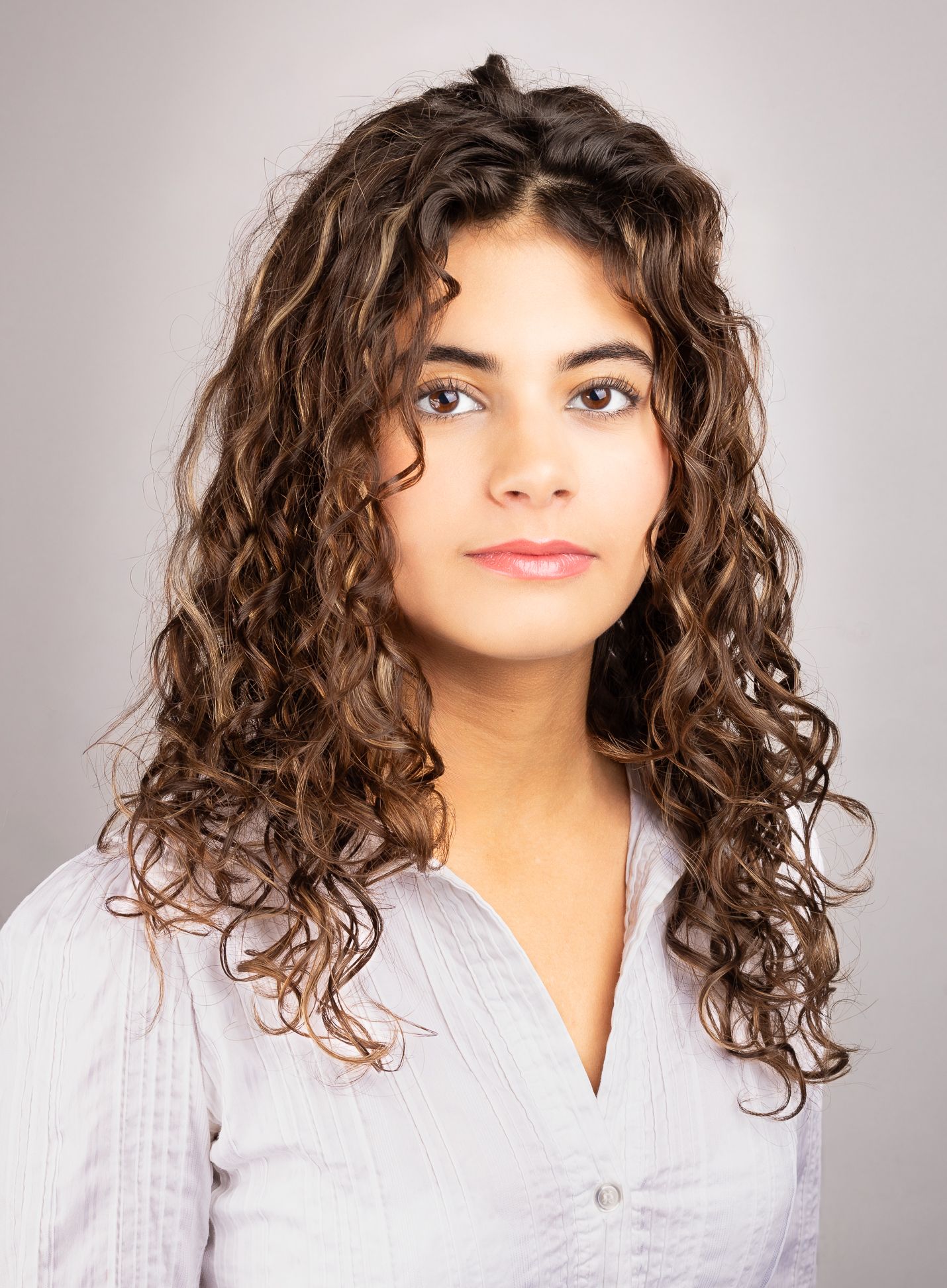 Headshot portrait of a girl in front of a white backdrop, half smile facial expression