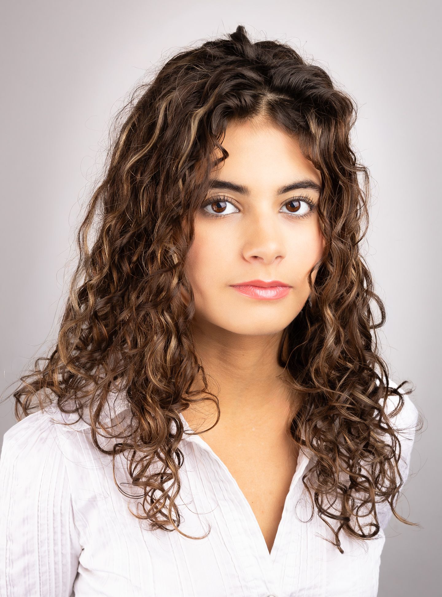 Headshot portrait of a girl in front of a white backdrop, neutral facial expression
