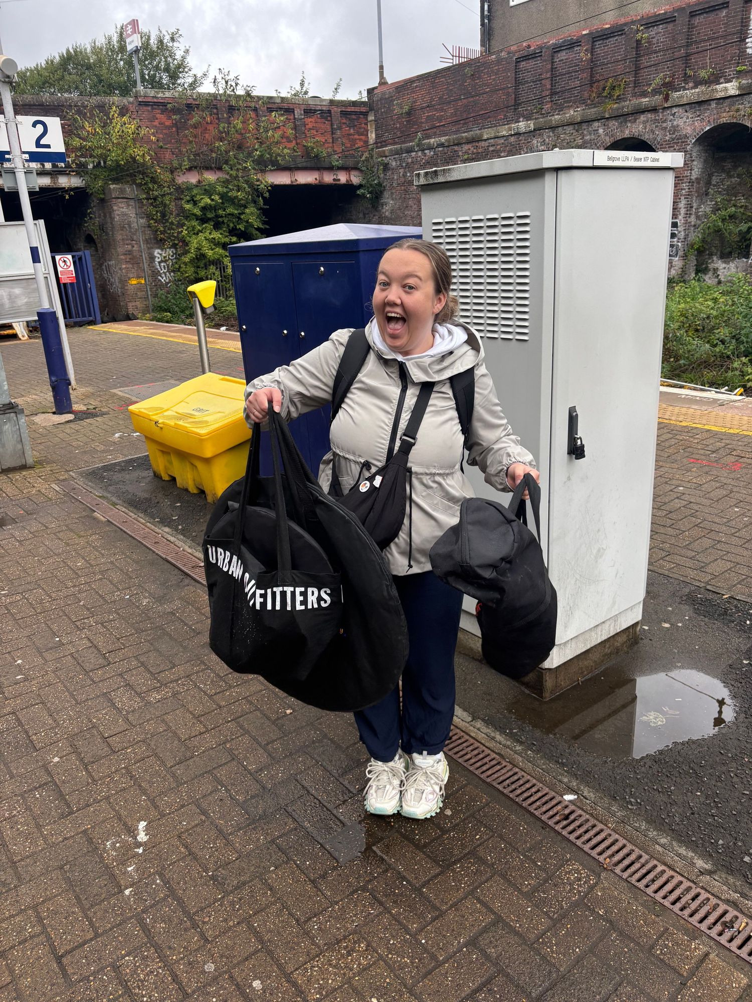 Woman laughing at train station holding Urban Outfitters bags.