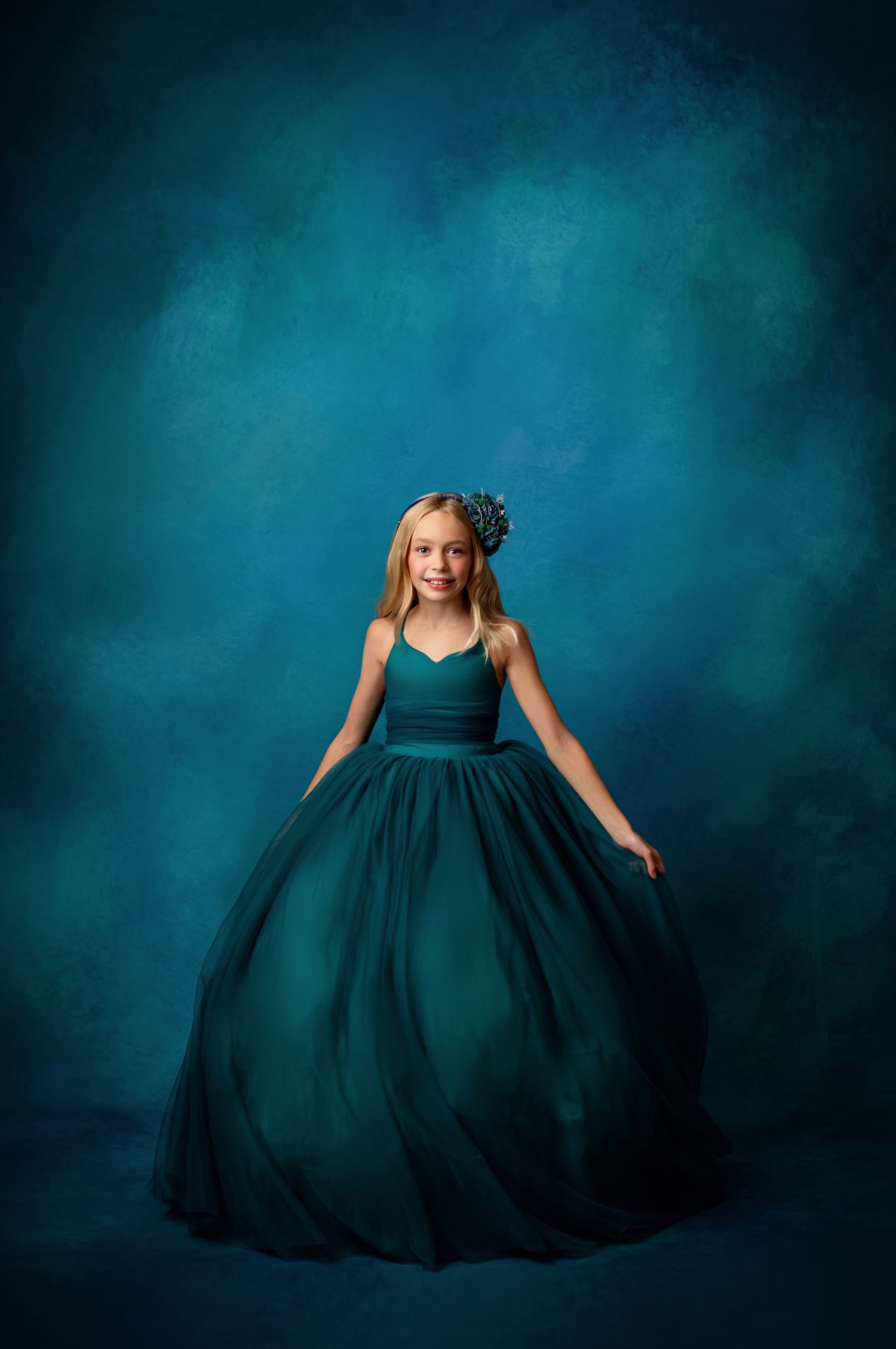 Elegant teal ball gown swirls dramatically against a misty blue-gray background in a dreamy portrait session.