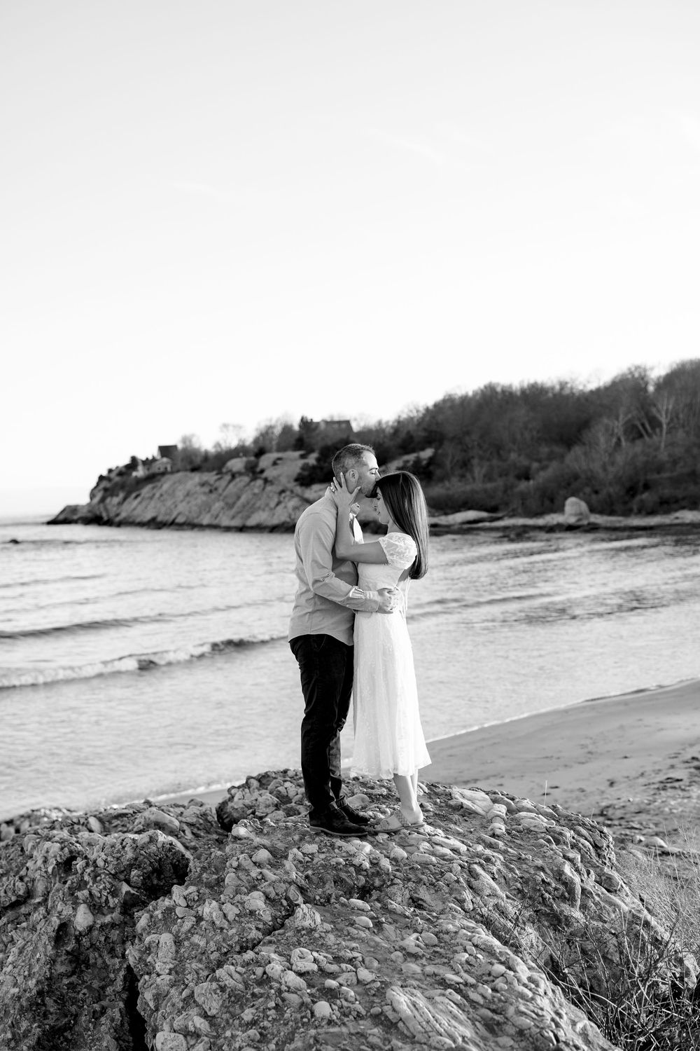 Couple embracing and kissing on rocky beach shore in black and white romantic portrait.