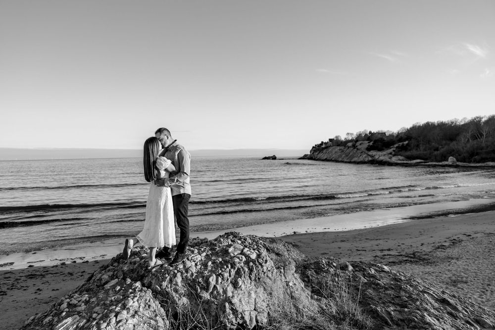 Black and white photo of a couple kissing on a rock at the beach during their romantic seaside wedding shoot.
