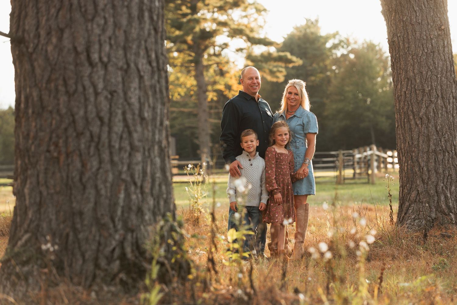 A group stands between tall trees in a park during golden hour as sunlight filters through the branches.