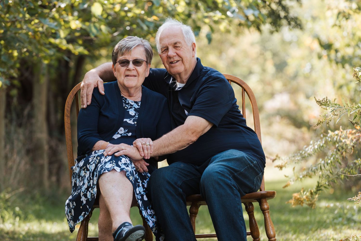 A couple sits together on a wooden bench in a sunlit garden setting during an outdoor photo session.