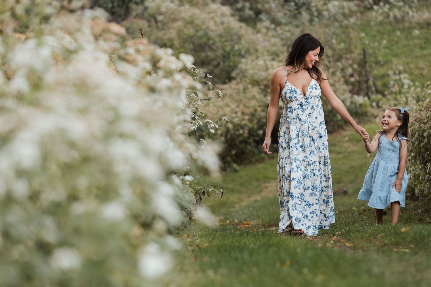 A mother and daughter walk through a blooming spring meadow wearing matching floral blue dresses.