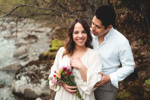 Smiling bride in cream dress holding colorful bouquet embraced by groom in nature setting.