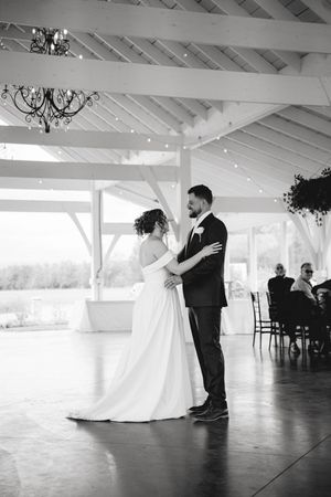 Black and white photo of a bride and groom sharing their first dance in an elegant venue with chandeliers.