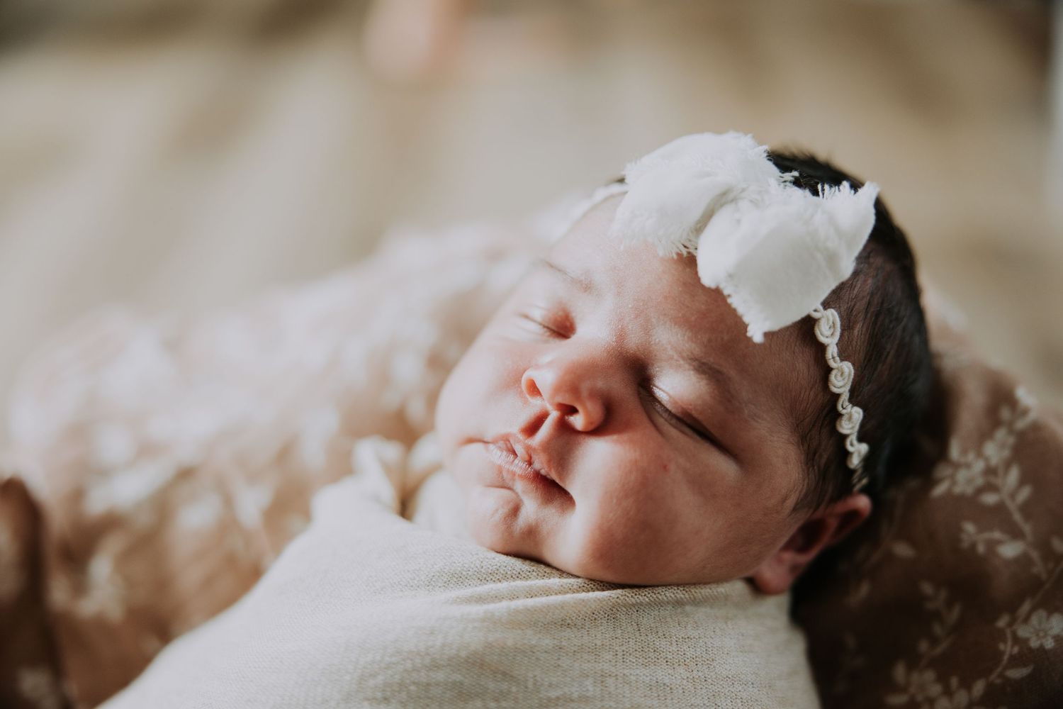 Peaceful newborn baby swaddled in white wrap, sleeping in a cozy basket with green blanket and chunky knit throw.