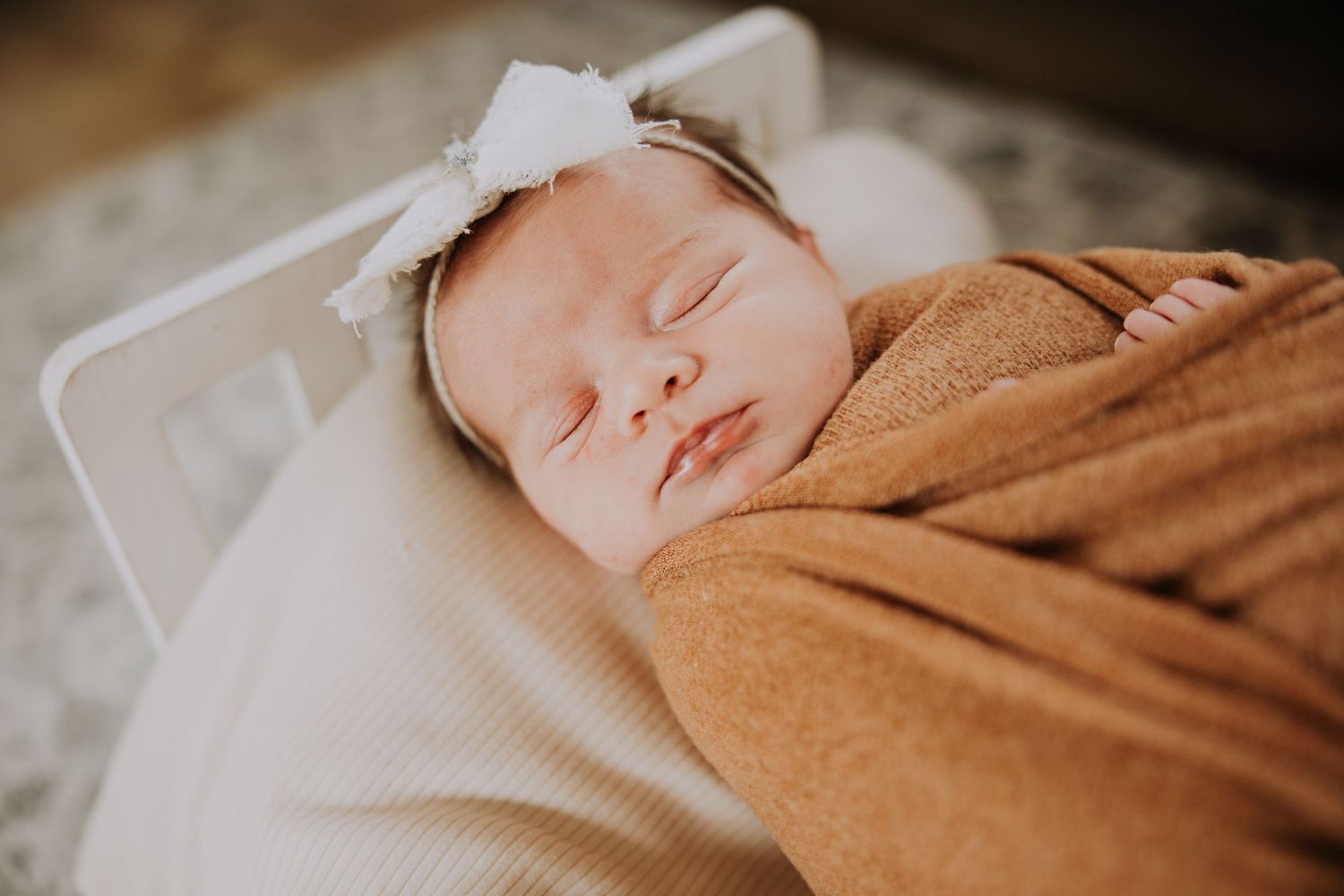 Peaceful newborn baby swaddled in white wrap, sleeping in a cozy basket with green blanket and chunky knit throw.
