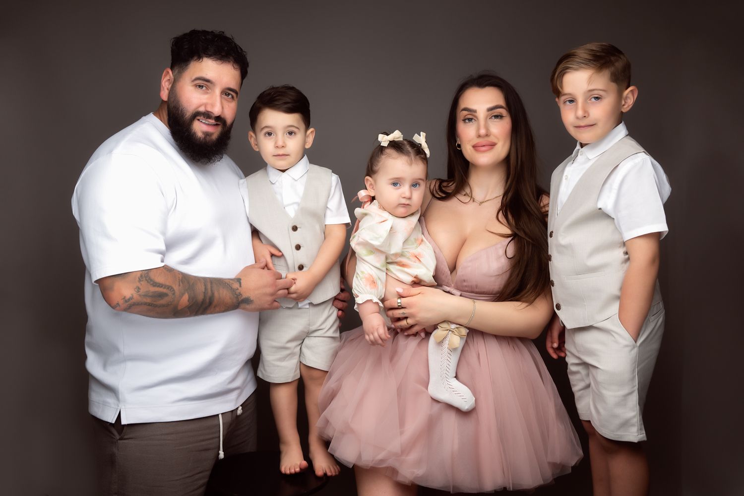 Family of five posing for a professional studio portrait, parents with two boys and a baby girl in elegant outfits.