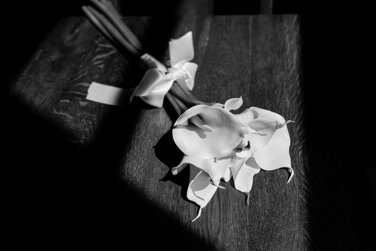 Black and white photo of elegant white calla lily boutonniere on a wooden surface.