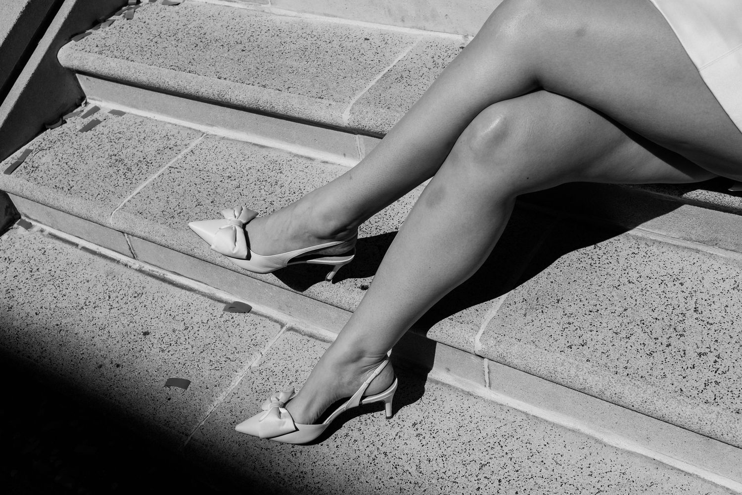 Black and white photo of a woman's legs in elegant heels resting on stone steps.