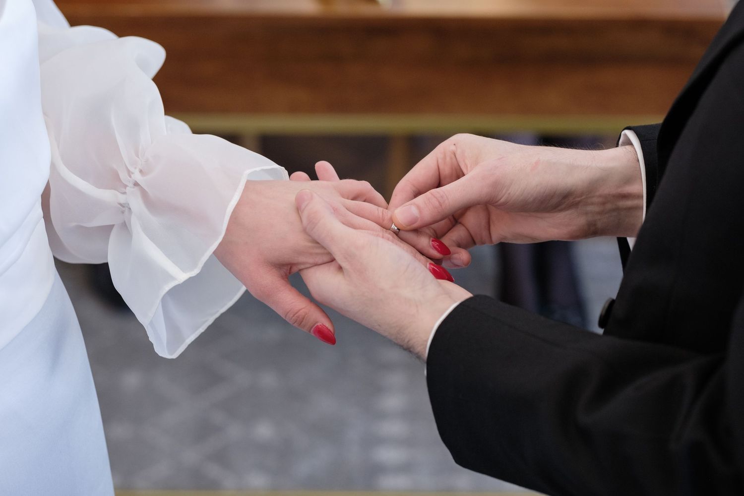 Close-up of a wedding ring exchange ceremony, bride in white dress with red nails receiving ring from groom.