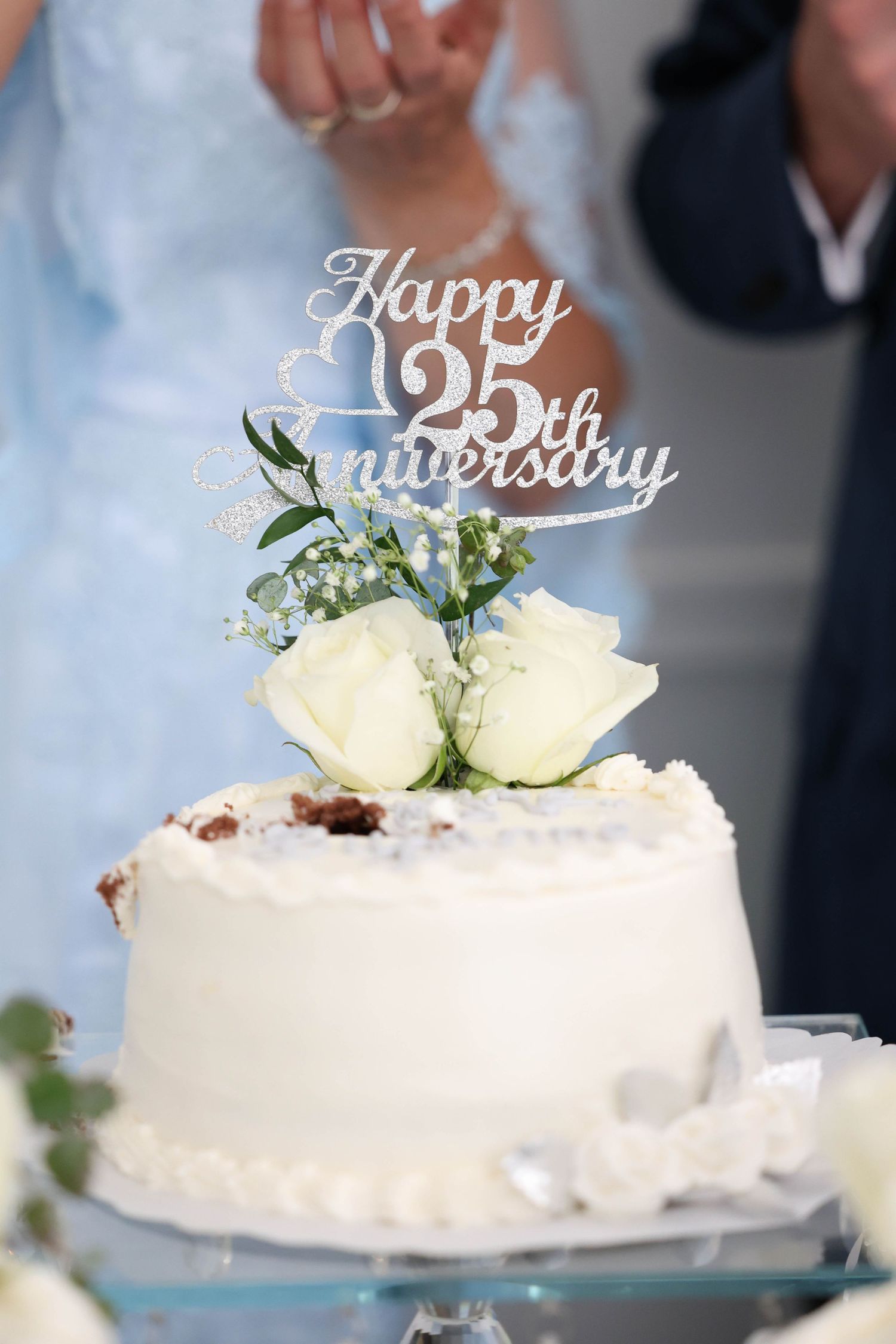 White anniversary cake with roses and Happy 25th Anniversary topper at a celebration.