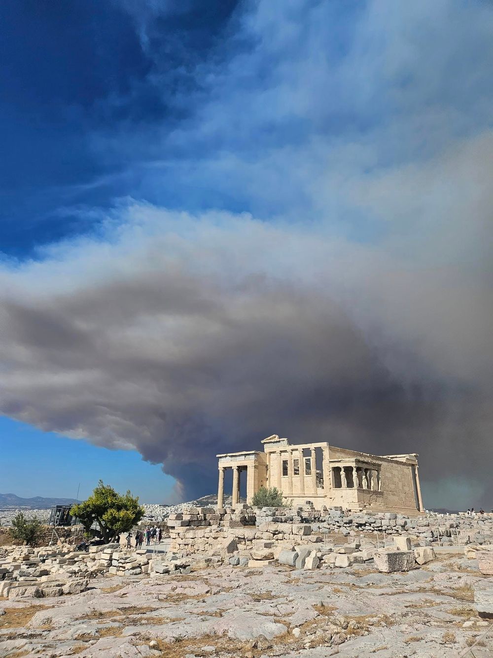 Ancient Greek Erechtheion temple on the Acropolis with dramatic wildfire smoke clouds filling the sky behind it.
