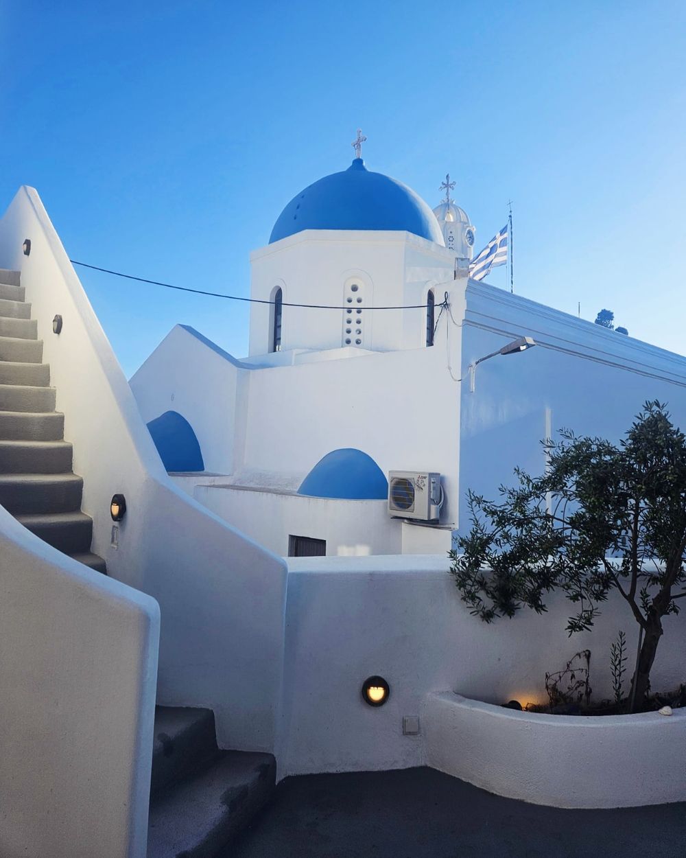 White-washed Greek church with blue domes and stairs under clear blue sky in Santorini, Greece.