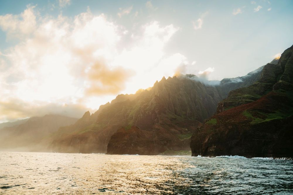 Dramatic Na Pali Coast cliffs bathed in golden sunset light over rough ocean waters in Kauai, Hawaii.