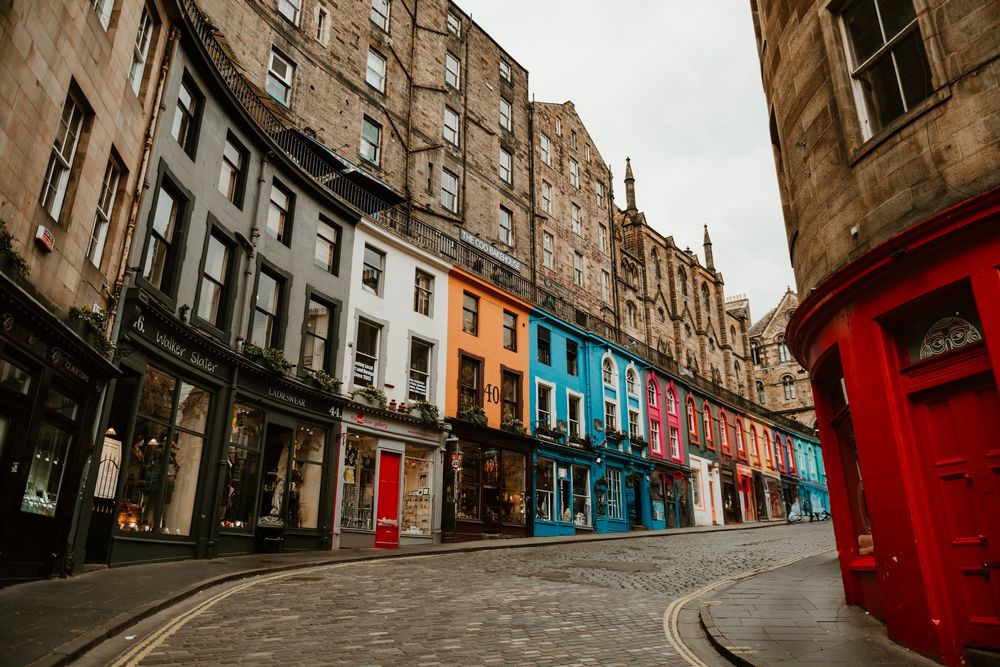Colorful historic shopfronts line a cobblestone street in Edinburgh's Victoria Street, Scotland.