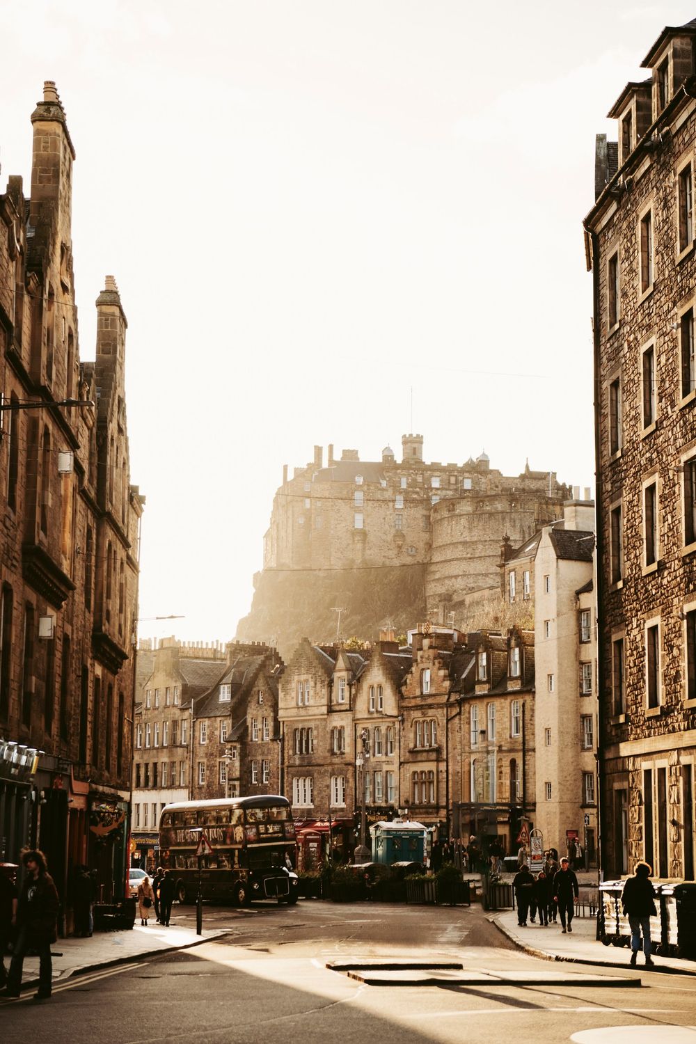 Sunlit Edinburgh street with historic stone buildings leading to Edinburgh Castle on a hazy morning.