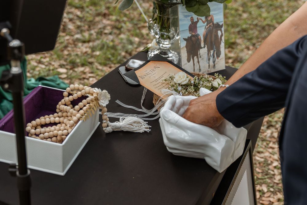 Wedding officiant in white gloves arranging ceremonial items on a decorated table outdoors.