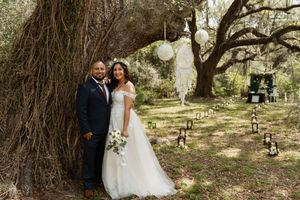 Bride and groom smiling together beside a grand tree with lanterns and wedding decor nearby.