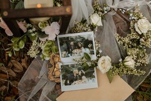 Polaroid wedding photos surrounded by white roses, greenery, and a bridal veil on the ground.
