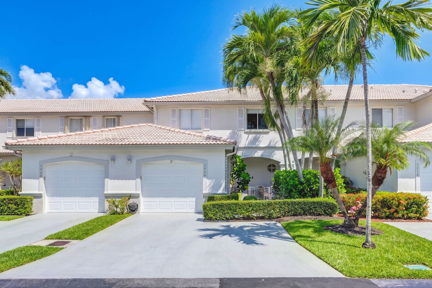 Two-story Florida home with white stucco exterior, two-car garage, palm trees, and manicured landscaping under blue skies.