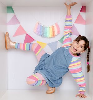Young girl in colorful striped outfit striking a fun pose inside a decorated pastel box with bunting.