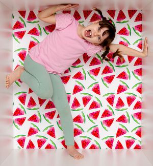 A joyful girl in pink top and green leggings poses on a vibrant watermelon-patterned white fabric background.