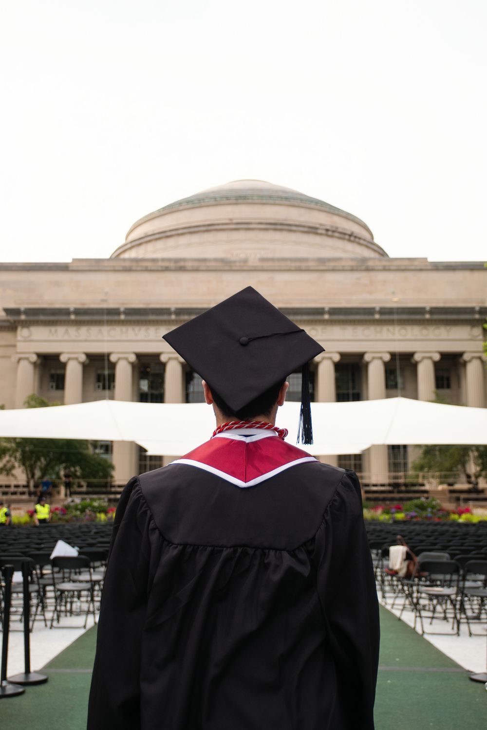 Graduate in black cap and gown stands before a grand domed university building during commencement ceremony.
