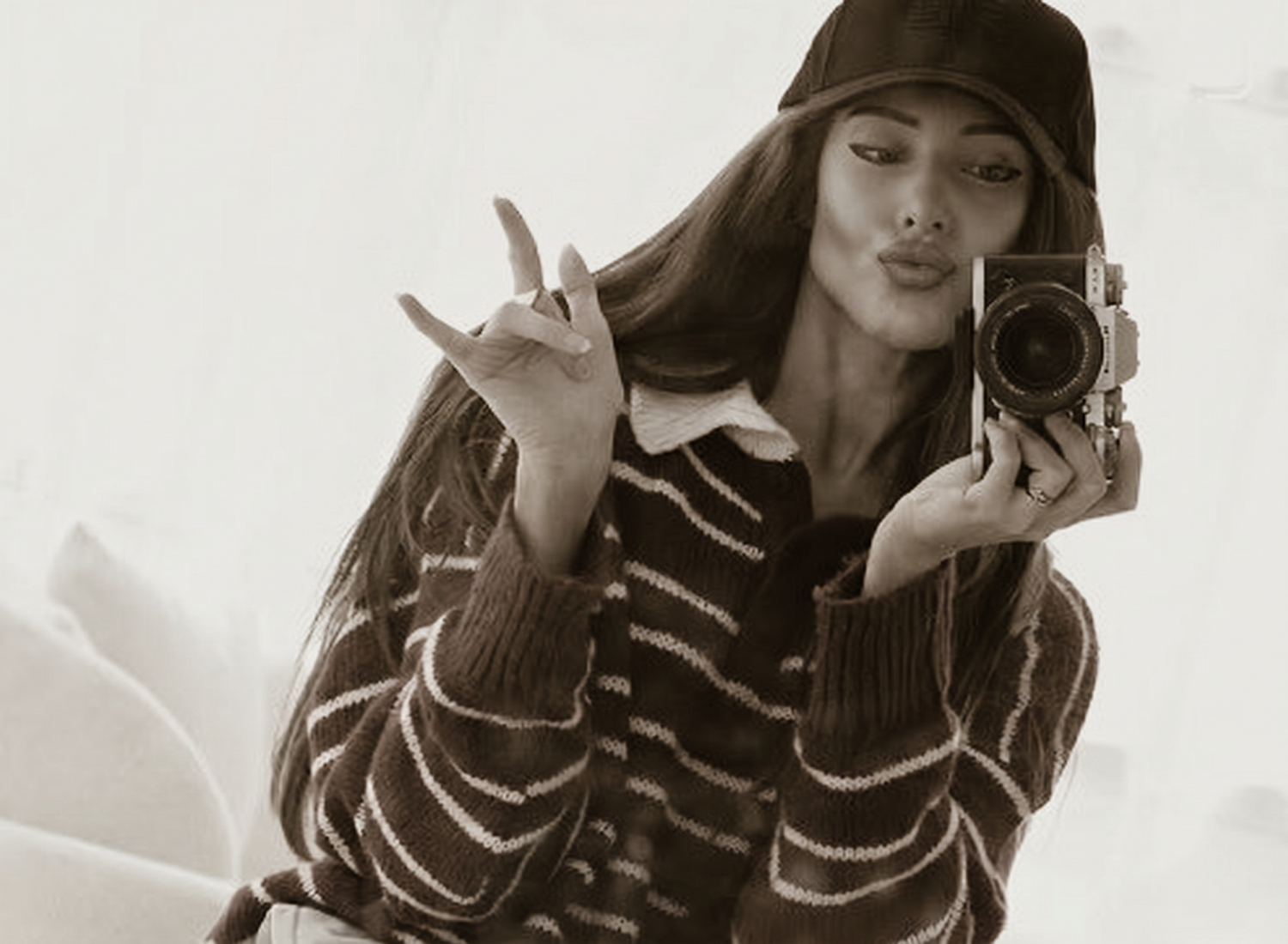 Woman in striped sweater and bucket hat poses with vintage camera in sepia-toned mirror selfie.