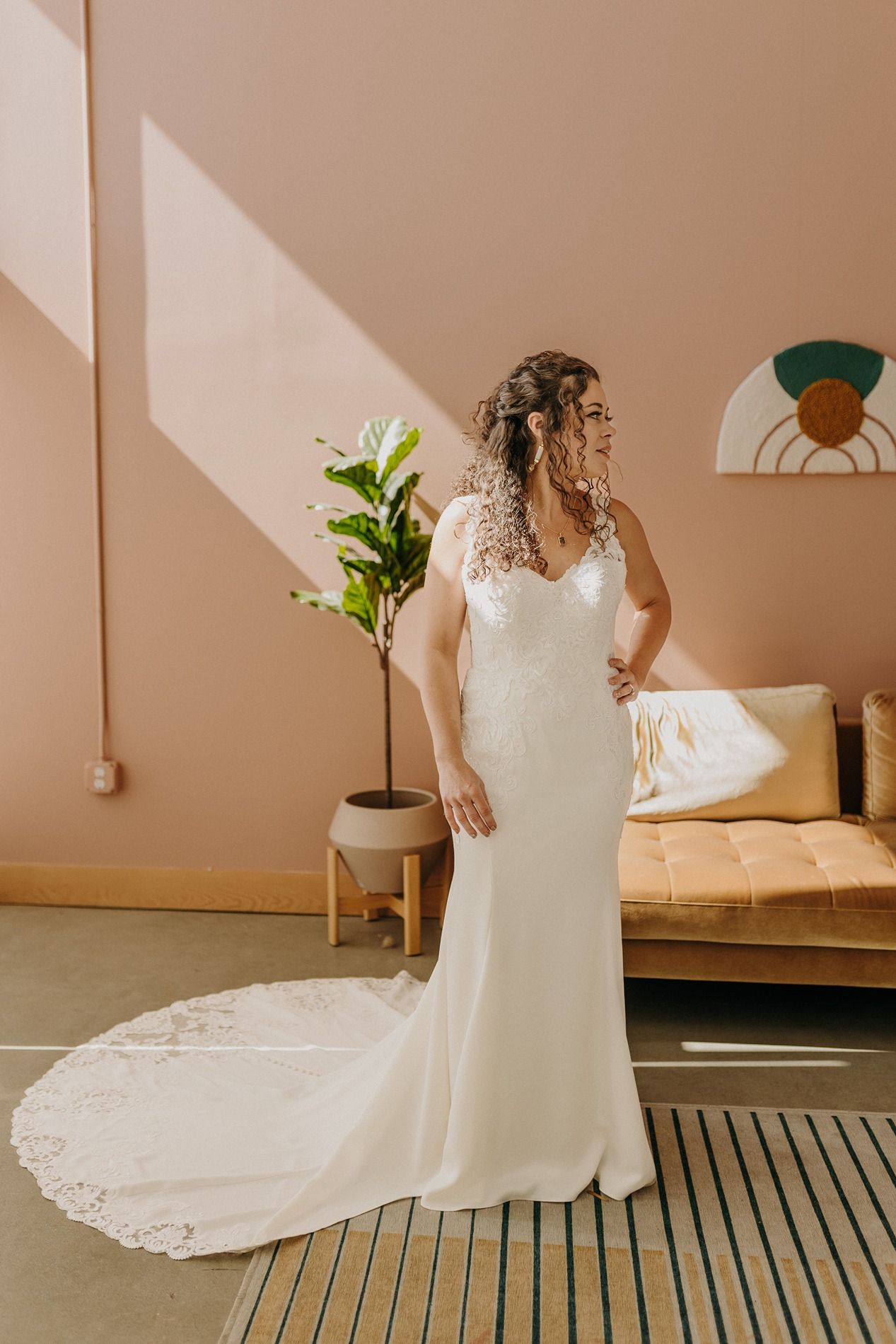 Bride in elegant white lace wedding gown with train posing in sunlit room with pink walls and modern decor at The Lane.