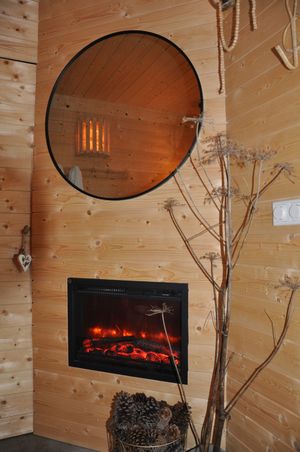 Cozy wooden cabin interior with electric fireplace, round mirror, and rustic pine cone decor.