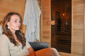 Woman relaxing in a cedar infrared sauna spa interior with warm lighting and hanging robe.