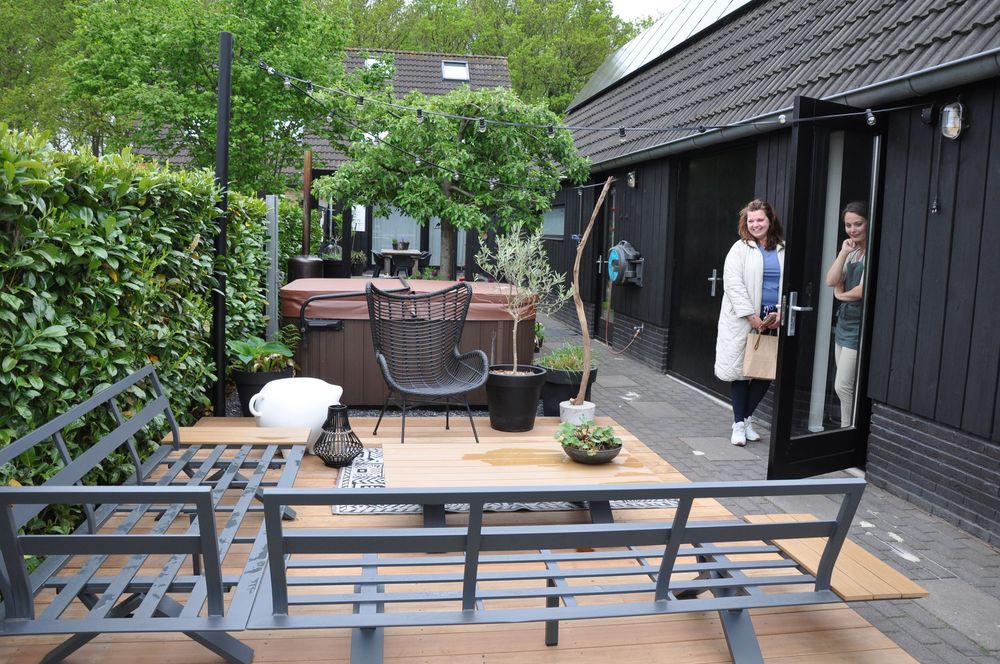 Exterior view of a modern dark-painted spa building with a hot tub on a wooden deck patio.