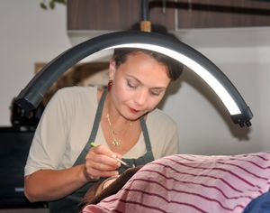 Esthetician in gray apron performing a facial treatment on a client under a professional arch lamp.