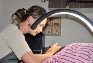 Close-up of esthetician leaning in to perform detailed facial treatment on client under arch lamp.