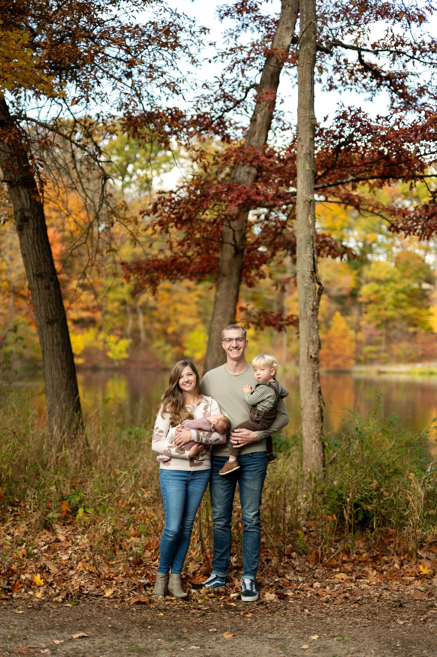 Couple standing on a wooden bridge surrounded by colorful autumn foliage in a forest setting.