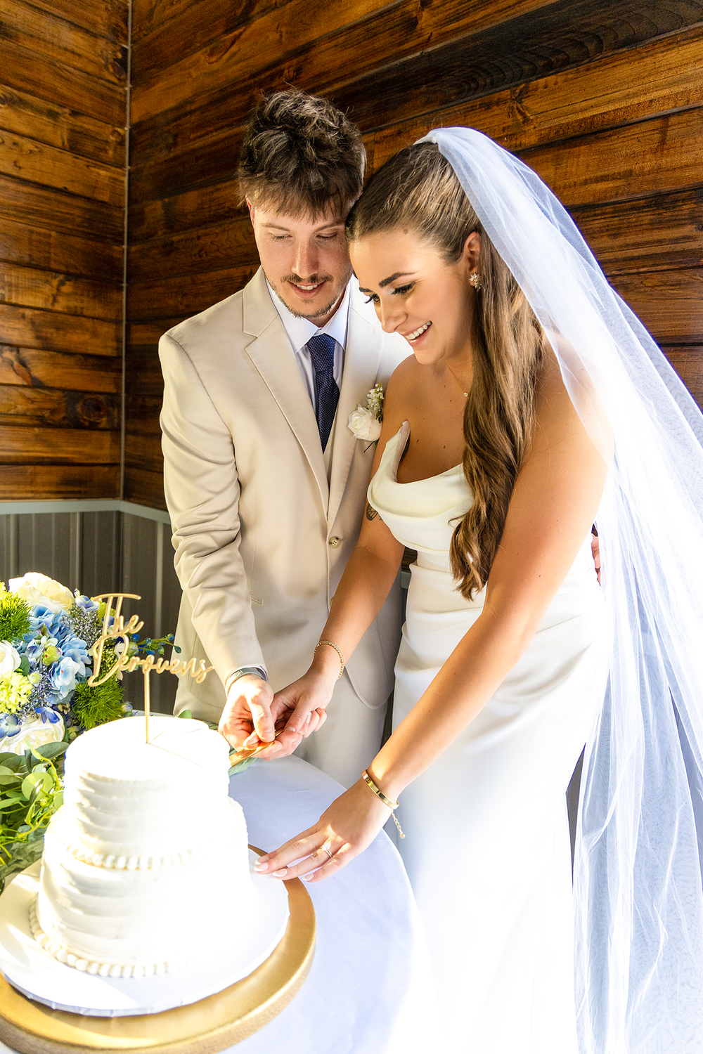 Bride and groom cutting their white tiered wedding cake topped with The Derouens gold cake topper.