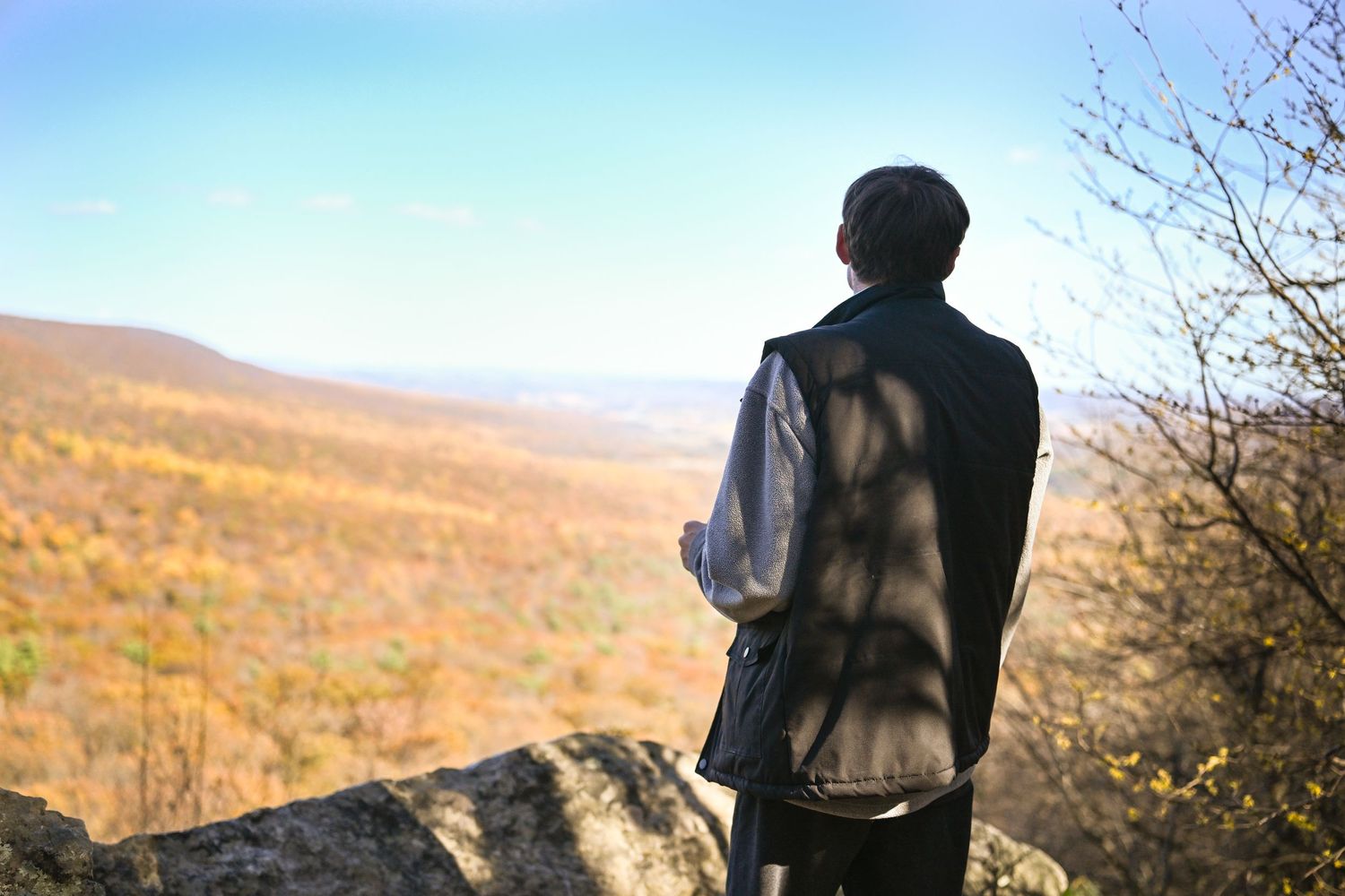 Photograph of a young man facing away from the camera with a vista in front of him and a breathtaking view of the valley below him