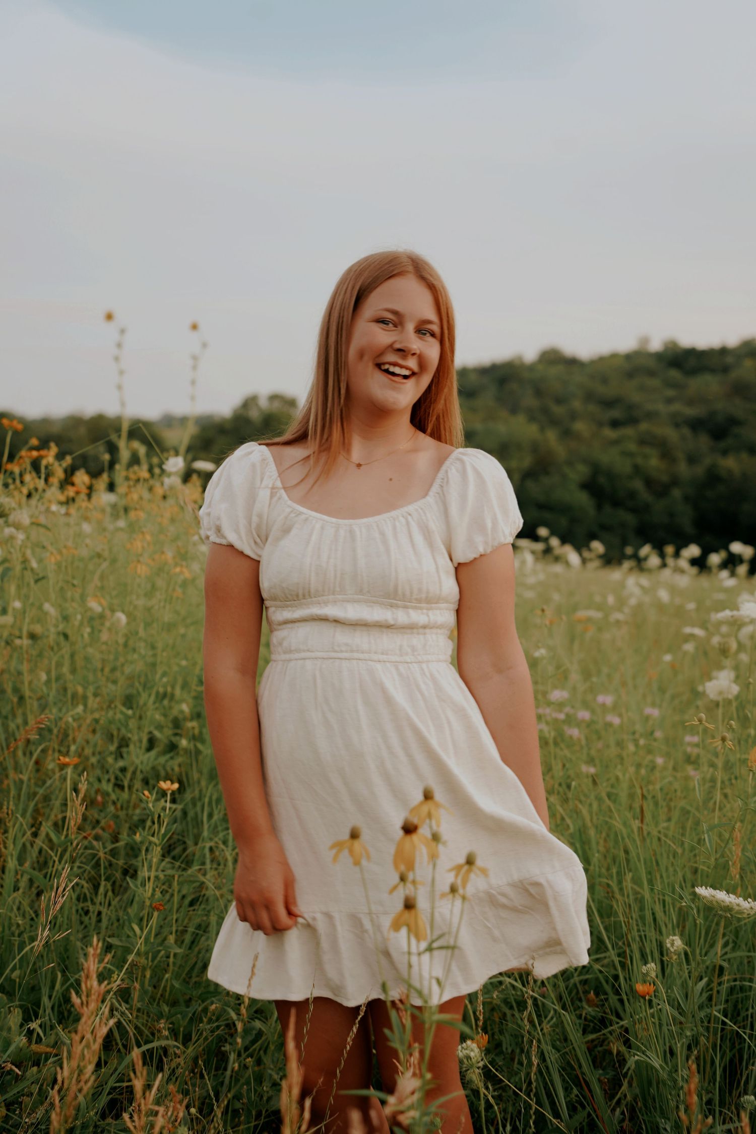 Happy young woman in white puff-sleeve dress laughing while standing in a golden wildflower field.