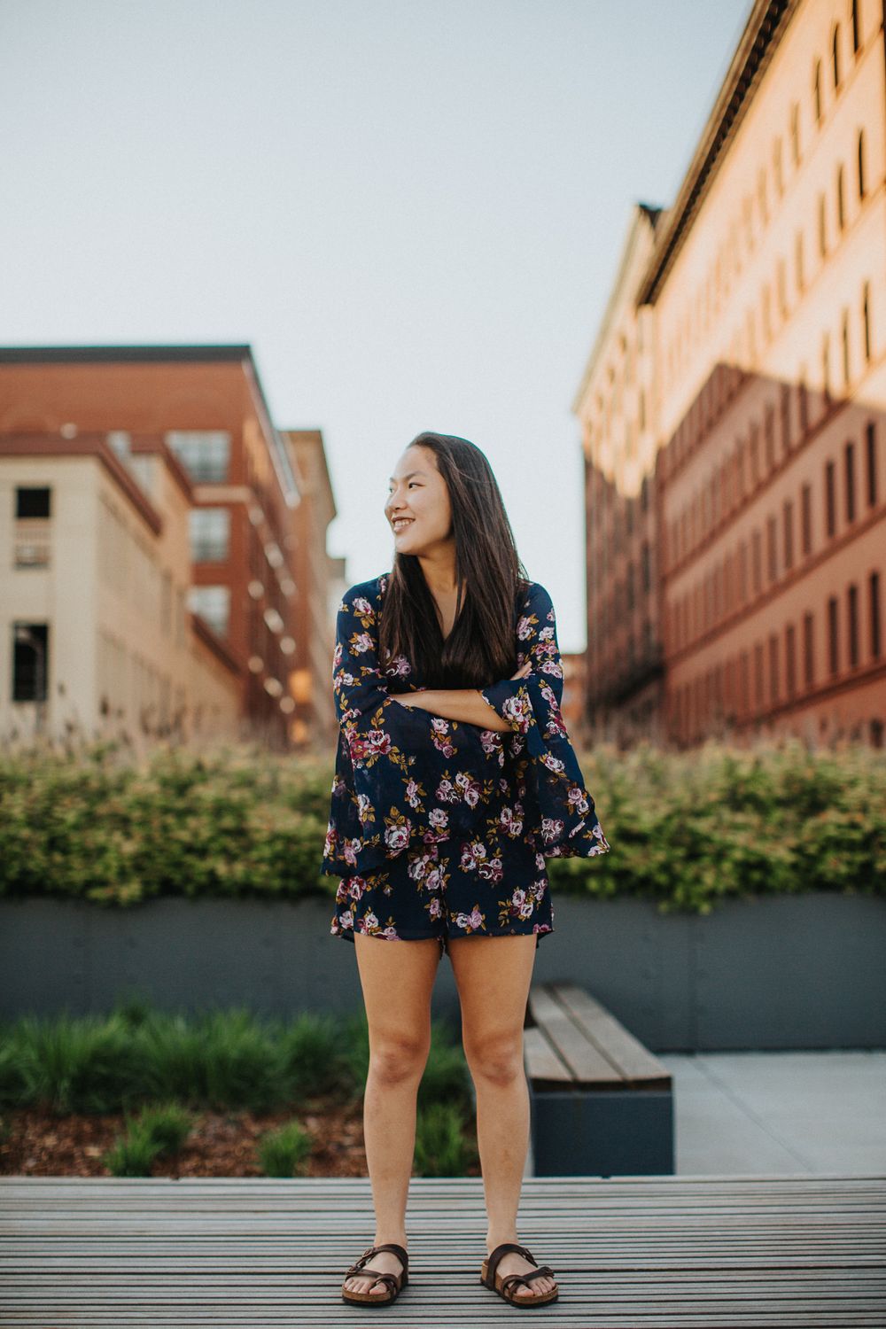 Person in floral dress sits on urban steps with brick buildings in background during golden hour lighting.