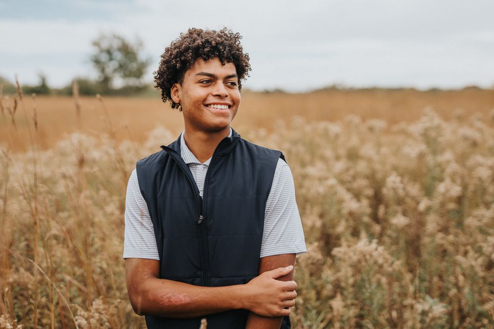 A person wearing a navy vest stands in a golden wheat field during sunset.
