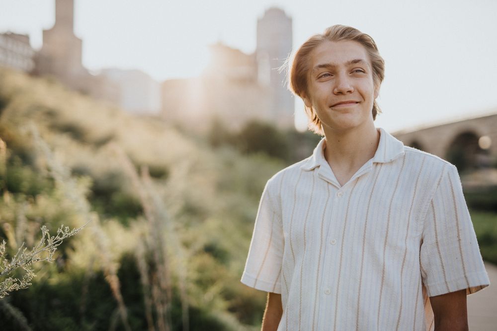 A person in a white striped shirt smiles while standing outdoors in warm sunlight.