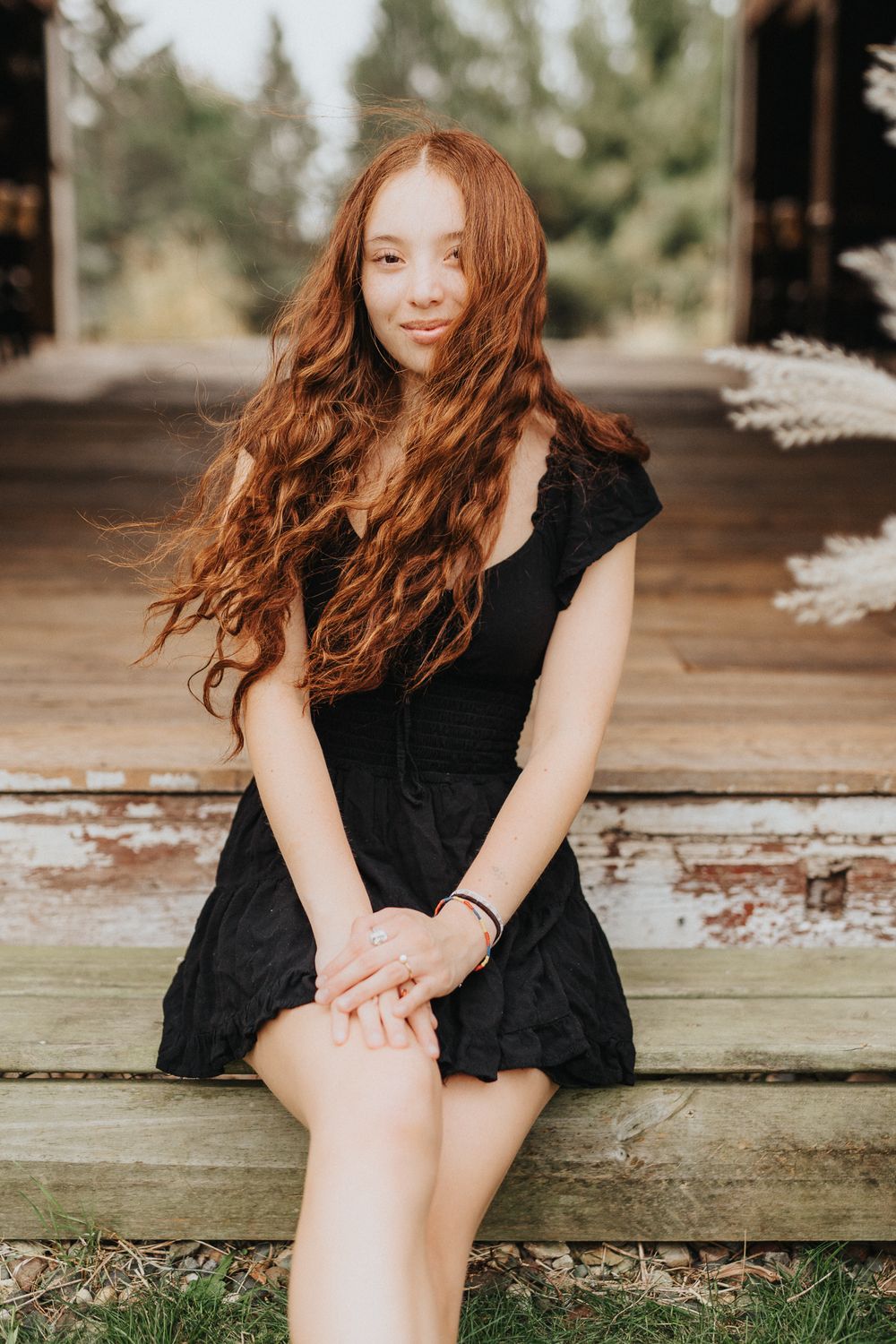 Woman in black dress sits on rustic wooden porch in outdoor portrait series.