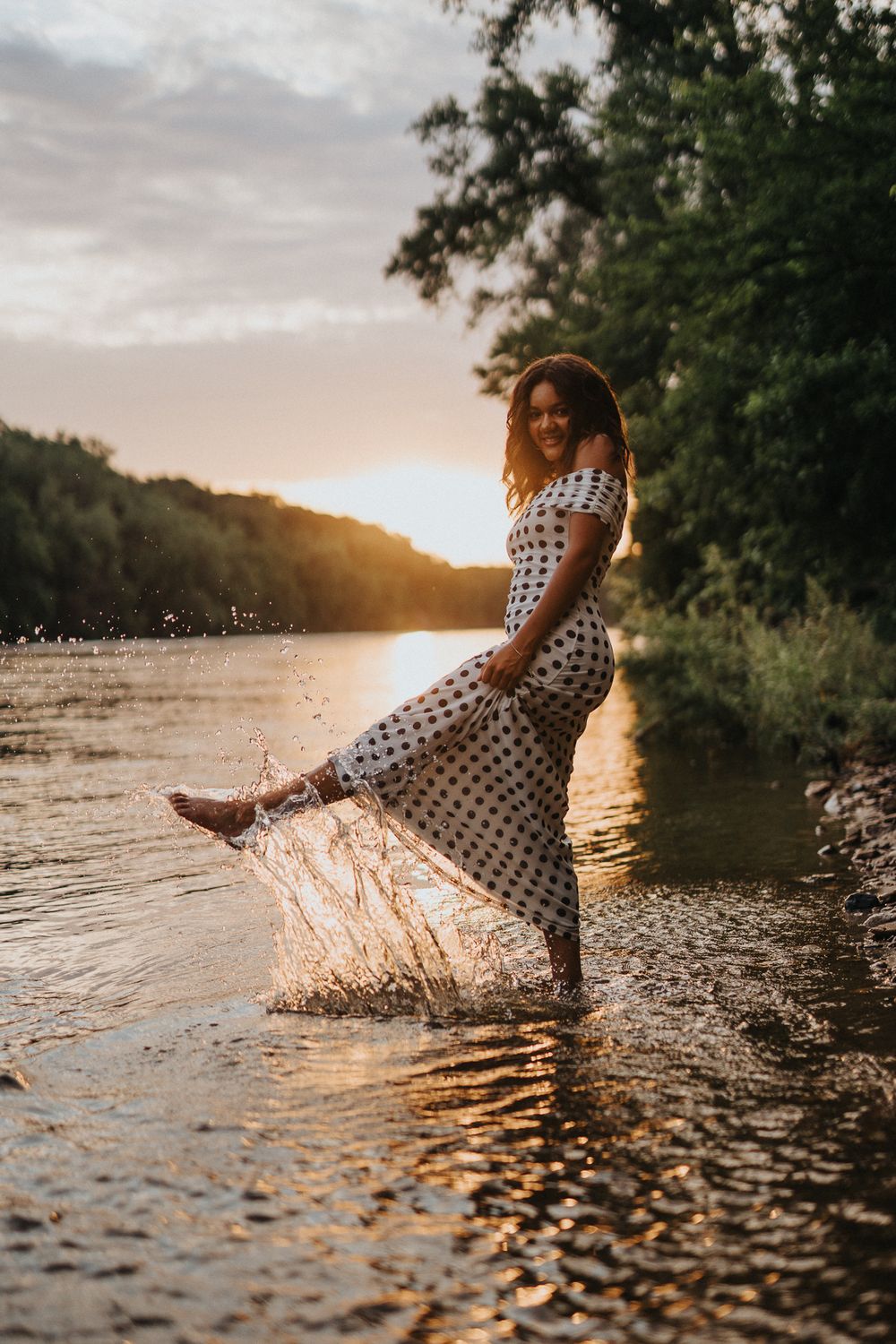 Someone in a polka dot dress splashes in shallow water during golden hour sunset creating magical water droplets.