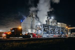 Large industrial equipment illuminated at night with steam rising near railway tracks.