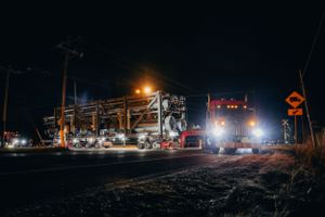Industrial equipment and trucks work on dark road with bright lights illuminating the scene.