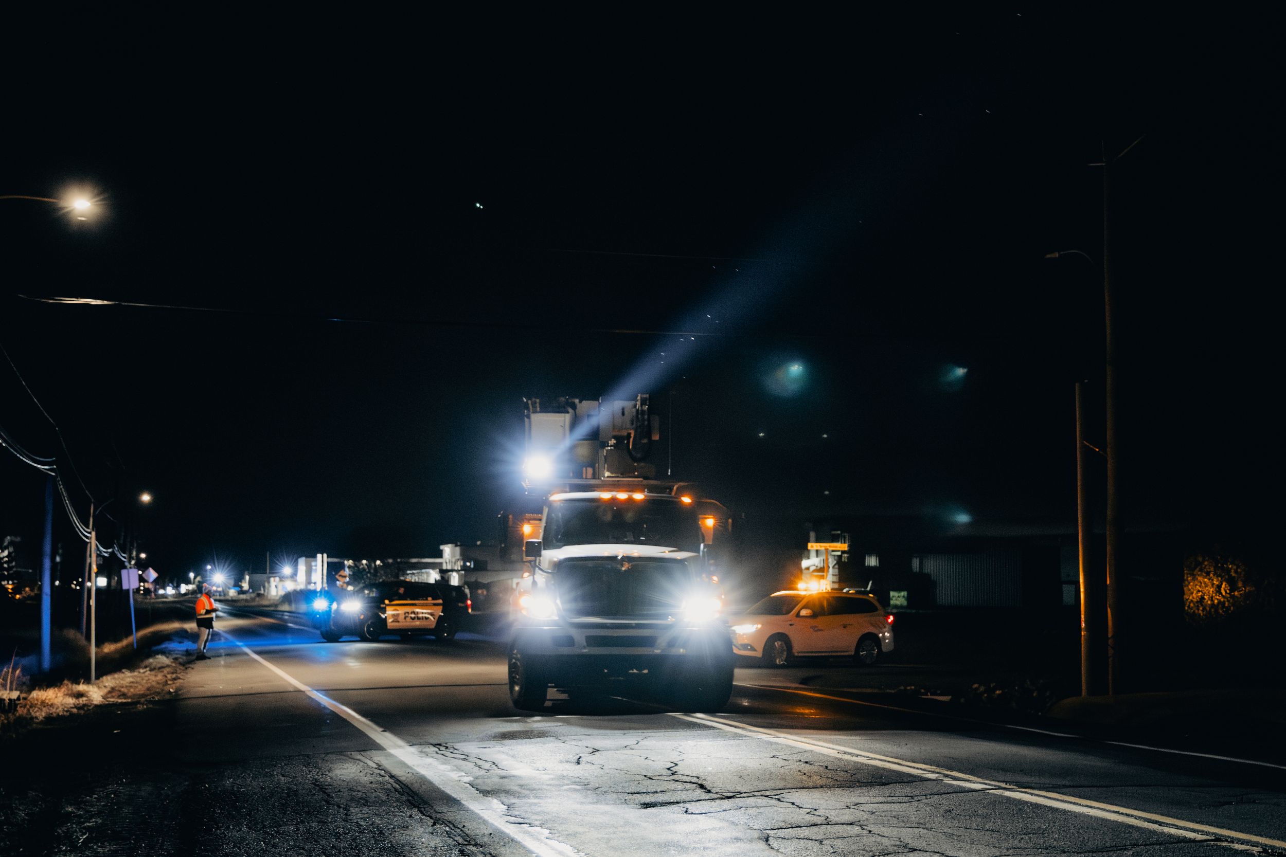 Bright headlights illuminate a dark suburban street at night.